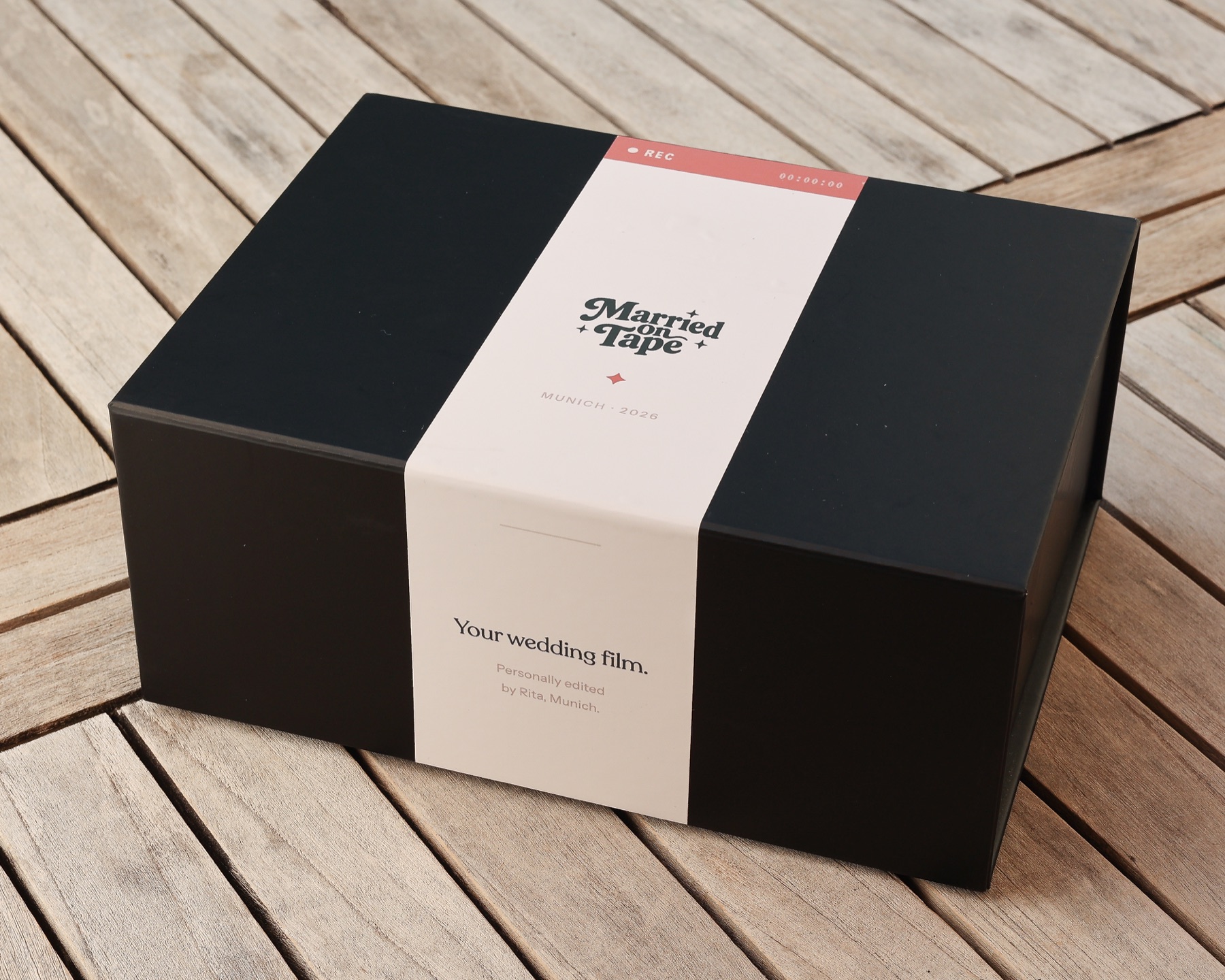 Die schwarze Married on Tape Versandbox mit gebrandetem Papierband auf einem Holztisch